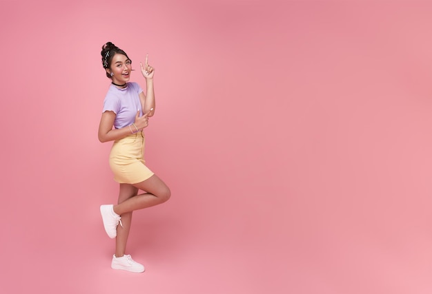 Felice giovane donna asiatica adolescente in piedi con il dito puntato isolato su sfondo rosa