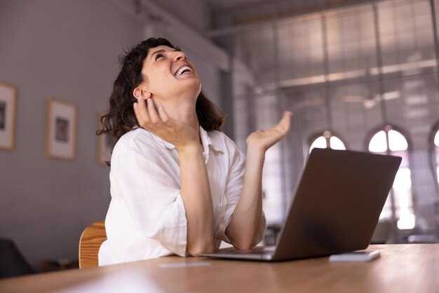 Felice giovane donna bruna caucasica in abiti casual ride con la testa seduta al tavolo con il computer portatile