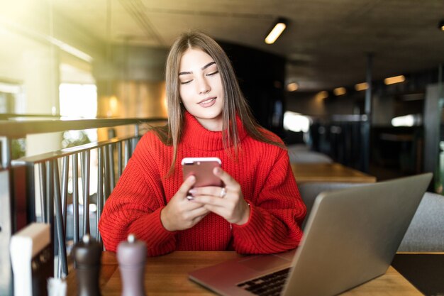 Felice giovane donna che utilizza laptop e smartphone al cafe