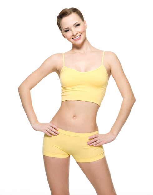 Felice giovane donna con bel corpo sottile in abiti sportivi gialli - isolato sul muro bianco