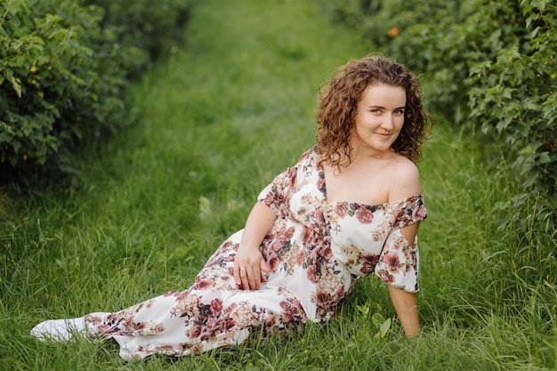 Felice giovane donna con i capelli ricci castani, indossa un abito, in posa all'aperto in un giardino