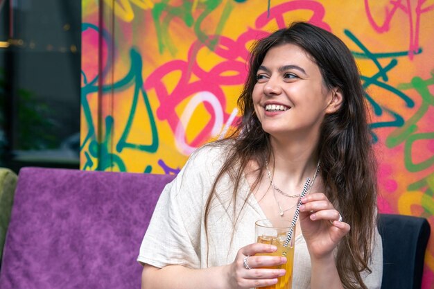 Felice giovane donna con un bicchiere di limonata contro un muro dipinto luminoso