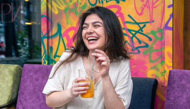 Felice giovane donna con un bicchiere di limonata contro un muro dipinto luminoso