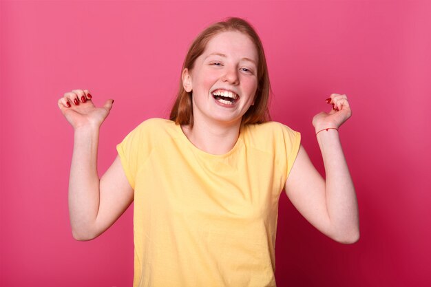 felice giovane donna emotiva in maglietta giallo brillante che ride sinceramente, tiene le mani in alto, sente una battuta divertente, si diverte a passare il tempo e divertirsi con i suoi amici. Concetto di emozioni di persone