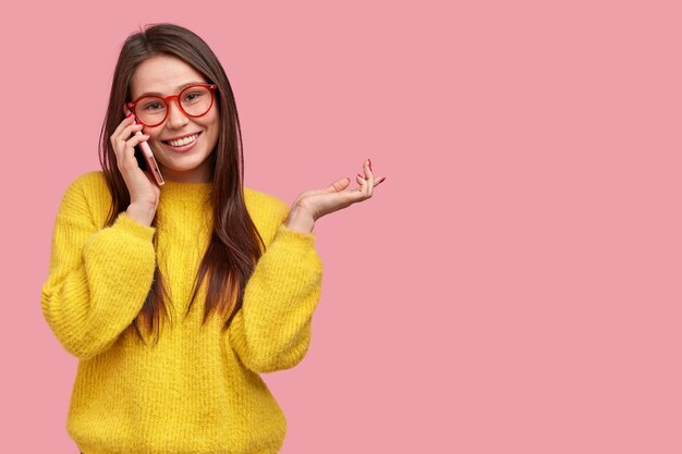 Felice giovane donna ha una conversazione telefonica con la migliore amica, gesticola attivamente mentre racconta cosa è successo con lei durante il giorno