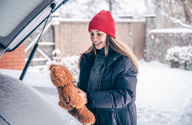 Felice giovane donna in inverno ha trovato un orsacchiotto nel bagagliaio di un'auto