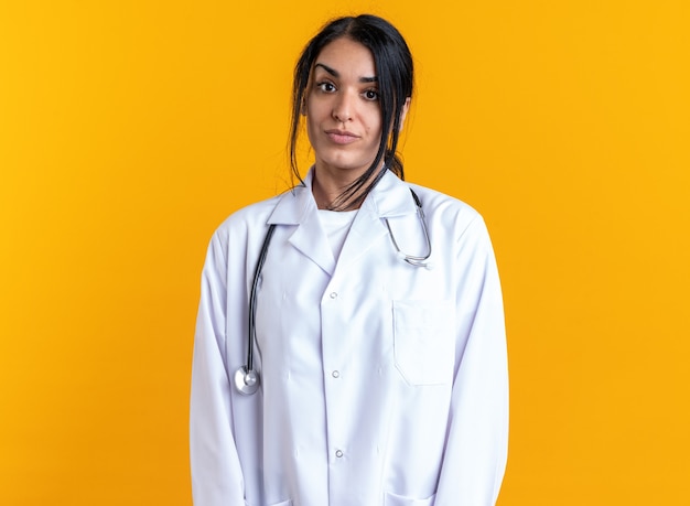 Felice giovane dottoressa che indossa una veste medica con uno stetoscopio isolato su una parete gialla