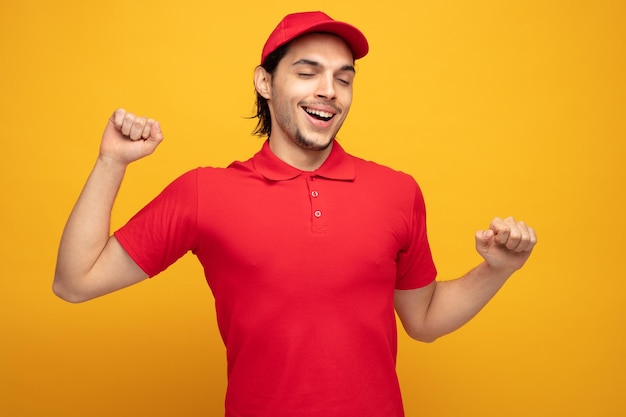 felice giovane fattorino che indossa uniforme e cappuccio tenendo i pugni in aria allungando sbadigliando e sorridendo con gli occhi chiusi isolati su sfondo giallo