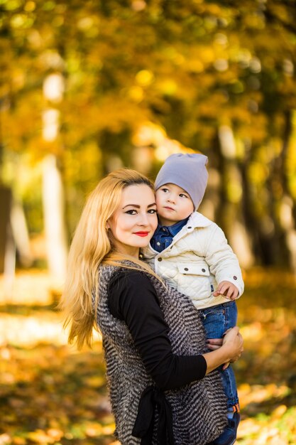 Felice giovane madre che gioca con il suo piccolo figlio bambino il sole caldo giorno d'autunno o d'estate. Bella luce del tramonto nel giardino delle mele o nel parco. Concetto di famiglia felice