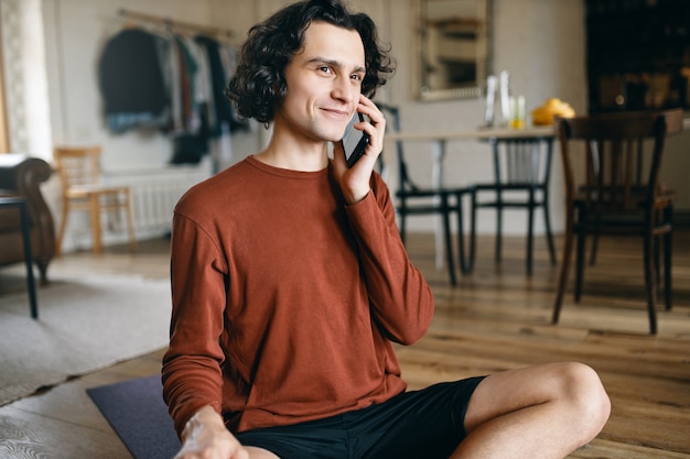 Felice giovane maschio in abiti casual che trascorrono tutto il giorno a casa da solo mentre le distanze sociali, sorridente