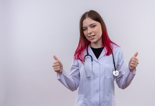 Felice giovane medico ragazza indossa stetoscopio abito medico i suoi pollici in su su sfondo bianco isolato con spazio di copia