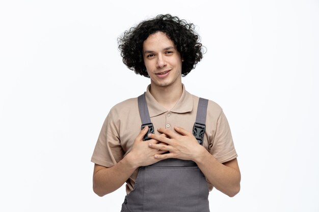 Felice giovane operaio edile maschio che indossa l'uniforme guardando la fotocamera che mostra un gesto di ringraziamento isolato su sfondo bianco