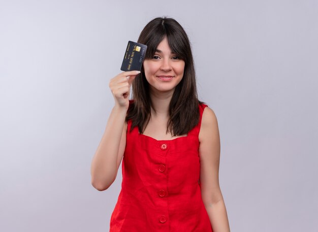 Felice giovane ragazza caucasica tenendo la carta di credito e guardando la fotocamera su sfondo bianco isolato