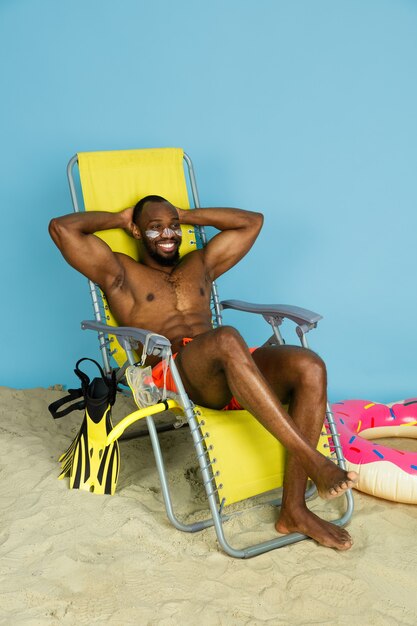 Felice giovane uomo che riposa e sorridente con anello da spiaggia come una ciambella su sfondo blu studio. Concetto di emozioni umane, espressione facciale, vacanze estive o fine settimana. Freddo, estate, mare, oceano.