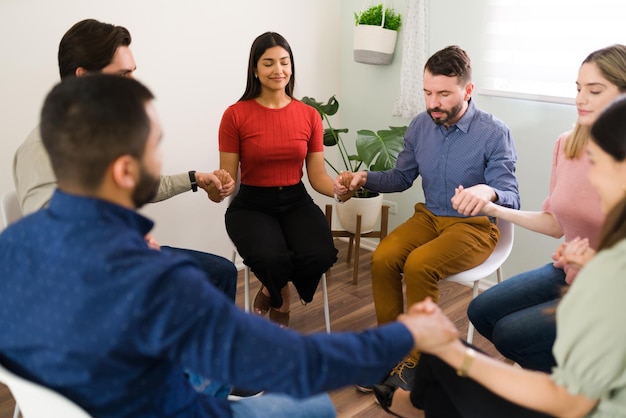 Felice gruppo eterogeneo di persone che si tengono per mano con gli occhi chiusi durante un incontro di riabilitazione per superare le loro dipendenze