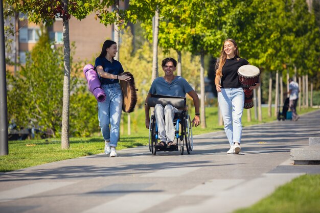 Felice handicappato uomo su una sedia a rotelle di trascorrere del tempo con gli amici che suonano musica strumentale dal vivo all'aperto.