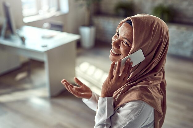 Felice imprenditrice islamica che fa una telefonata mentre lavora in ufficio