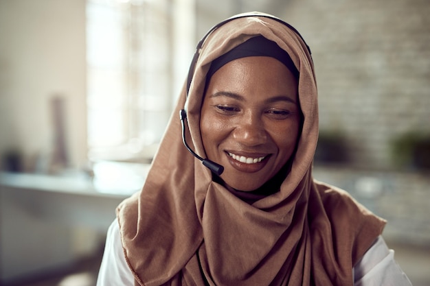 Felice imprenditrice islamica che indossa un auricolare mentre lavora in ufficio