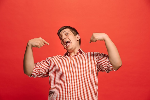 Felice l'uomo soddisfatto in piedi e sorridente isolato su sfondo rosso studio che punta a se stesso. Bellissimo ritratto maschile a mezzo busto. Giovane uomo emotivo.