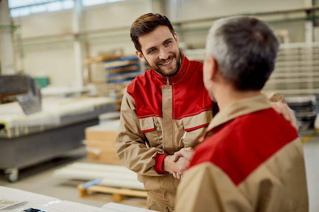 Felice lavoratore manuale che stringe la mano mentre lavora in officina di falegnameria