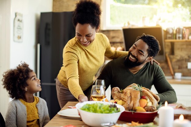 Felice madre nera che serve insalata alla sua famiglia durante il pasto del Ringraziamento a casa