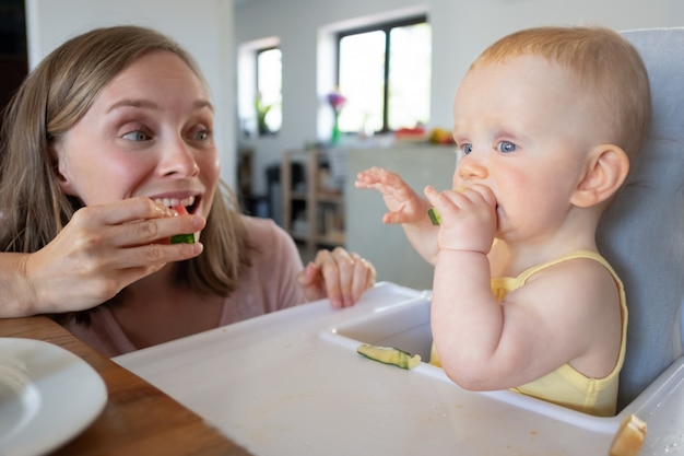 Felice mamma eccitata addestra il bambino a mordere cibi solidi, mangiando anguria insieme alla figlia. Colpo del primo piano. La cura dei bambini o il concetto di nutrizione