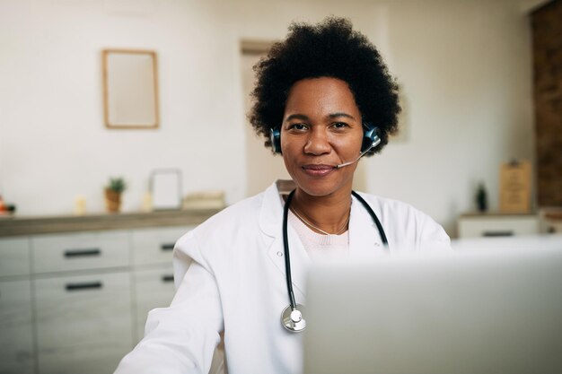 Felice medico afroamericano con auricolare che lavora al computer portatile nel suo ufficio