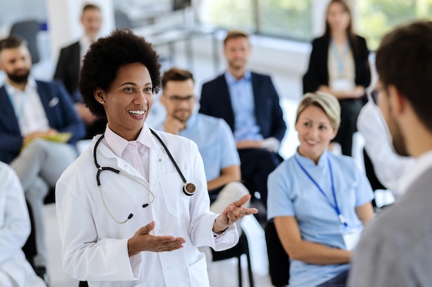 Felice medico nero che parla con un presentatore durante un evento educativo al centro congressi