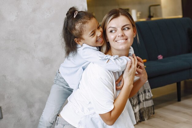 Felice piccola ragazza afroamericana che si arrampica sulle spalle della madre bionda sorridente. Madre e figlia che si abbracciano.