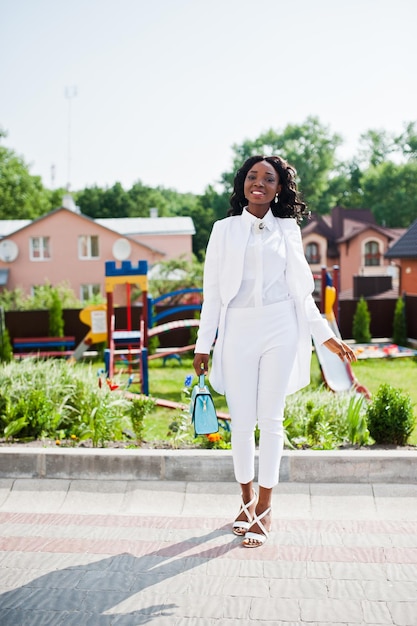 Felice ragazza afroamericana in abito bianco nel parco giochi sullo sfondo della città