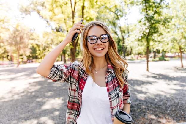 Felice ragazza bianca in bicchieri scintillanti trascorrere del tempo nel parco. Modello femminile adorabile con capelli biondi che godono del fine settimana di primavera.