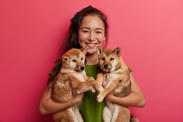 Felice ragazza bruna adotta due cuccioli dal rifugio, felice di avere nuovi amici, tiene animali domestici, essendo amante dei cani, andando a camminare. Il proprietario dell'animale suggerisce di adottare l'animale domestico, i sorrisi hanno volentieri rapporti amichevoli