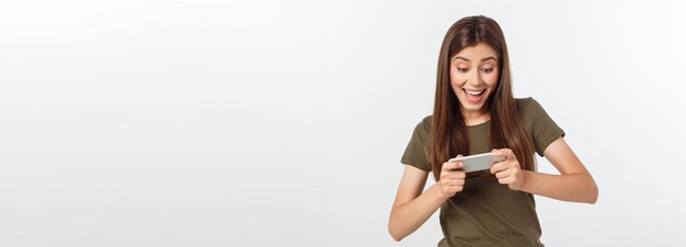 Felice ragazza bruna attraente gioendo vincere nel videogioco su smartphone isolato su sfondo grigio