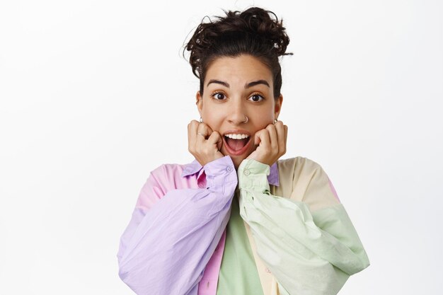 Felice ragazza sorpresa sorridente, ansimante stupita, guardando eccitata alla telecamera, cuore incredibile buone notizie, gioendo e festeggiando, in piedi su sfondo bianco.