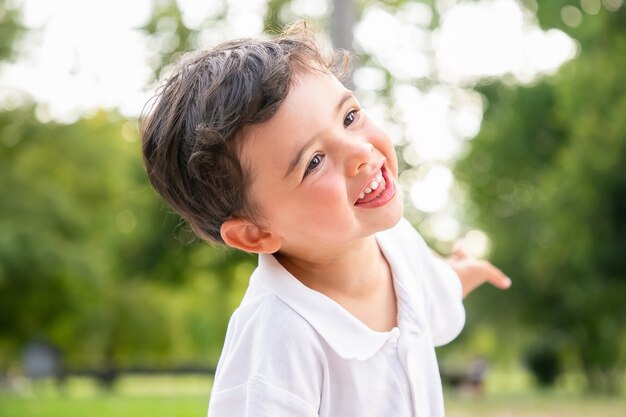 Felice ragazzo adorabile divertente ballare, ridere, divertirsi nel parco estivo, sorridere e distogliere lo sguardo. Colpo del primo piano. Concetto di infanzia