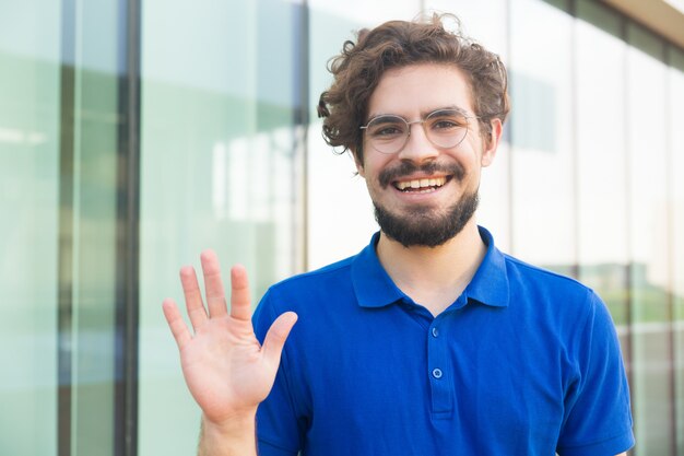 Felice ragazzo amichevole con gli occhiali, salutando con la mano