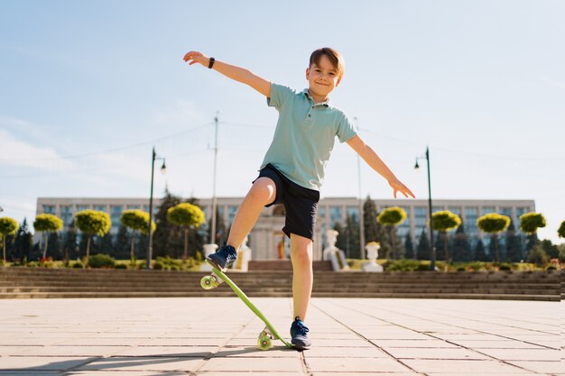 Felice ragazzo giocando su skateboard nel parco, bambino caucasico cavalcando penny board, praticare skateboard.