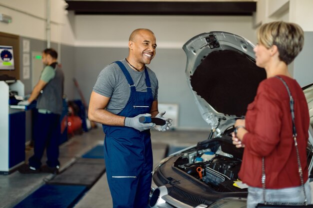 Felice riparatore auto afroamericano che parla con il cliente in un'officina