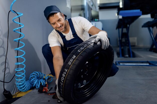 Felice riparatore che controlla il pneumatico dell'auto presso l'officina di servizio