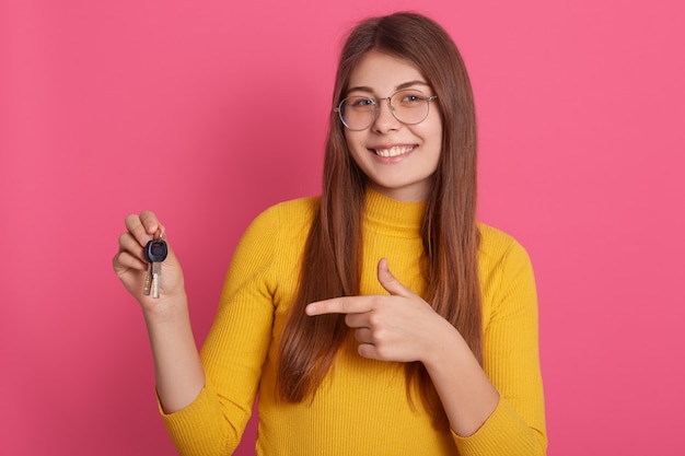 Felice sorridente femmina abiti casualmente, tenendo in mano le chiavi della macchina o del nuovo appartamento, indicando la chiave con il suo indice