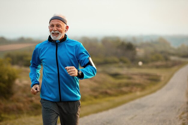 Felice sportivo senior che si sente motivato mentre ascolta musica e corre in natura Spazio di copia