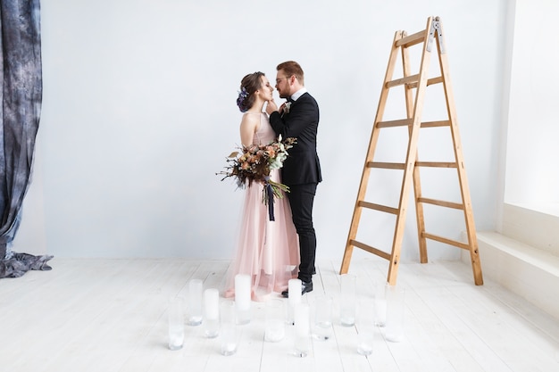 Felice sposa e lo sposo sulla scala in studio. Sfondo muro bianco isolato