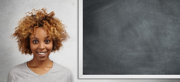 Felice studente africano con acconciatura afro in piedi isolato contro lavagna vuota con copia spazio per il contenuto pubblicitario con espressione gioiosa, ottenendo A a lezione di matematica