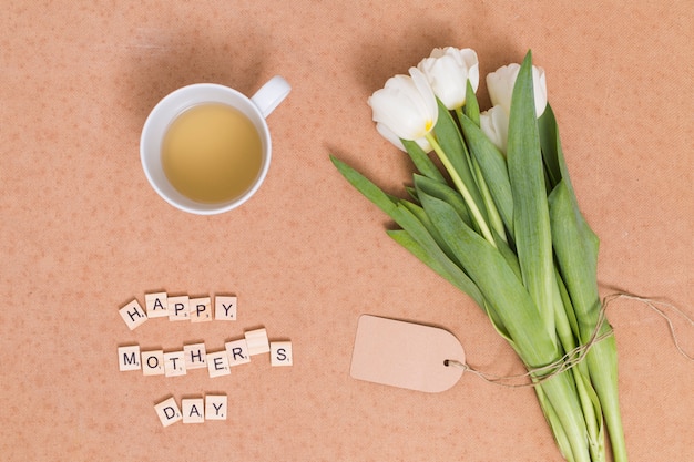Felice testo della festa della mamma; tè al limone con fiori di tulipano bianco su sfondo marrone