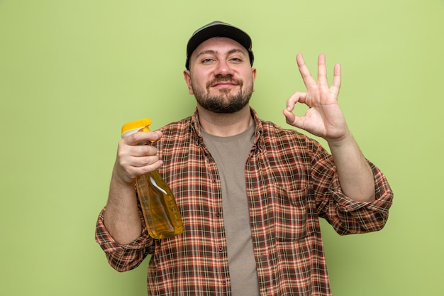 Felice uomo delle pulizie slavo che tiene in mano un detergente spray e fa un gesto ok segno