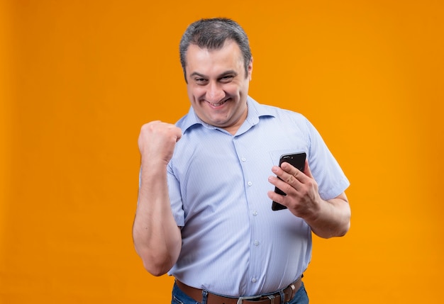 Felice uomo di mezza età in camicia a righe verticali blu e alzando la mano nel gesto del pugno chiuso