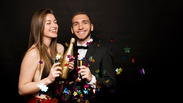 Felice uomo e donna con bottiglia e bicchieri di bevande tra i coriandoli