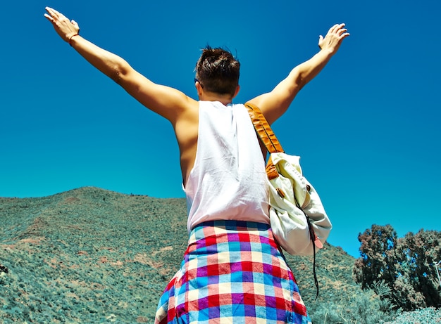 Felice uomo elegante in abiti casual casual saltando davanti alla montagna con le mani sollevate al sole e celebrando il successo