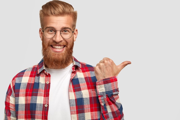 Felice uomo positivo con barba e baffi lunghi e spessi allo zenzero, ha un sorriso amichevole, vestito con una camicia a scacchi