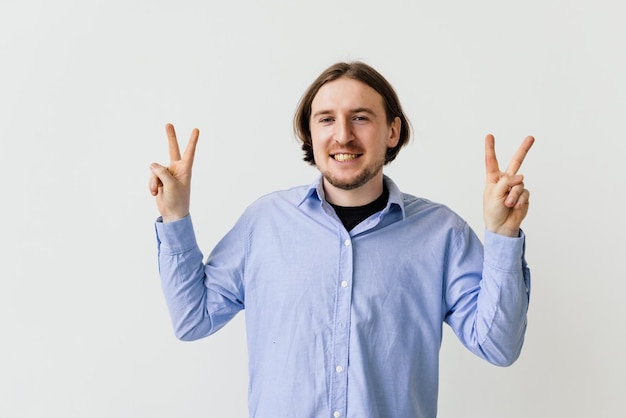 Felice uomo soddisfatto che mostra v segno simbolo di pace con le dita guardando la fotocamera con un sorriso a trentadue denti che celebra la sua vittoria di successo isolata su sfondo bianco